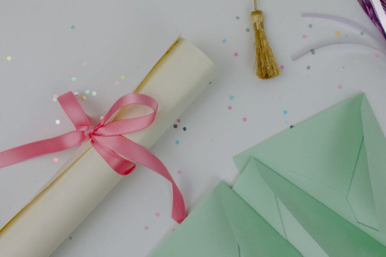 Flat lay of a decorative diploma with a pink ribbon, surrounded by confetti and green envelopes.
