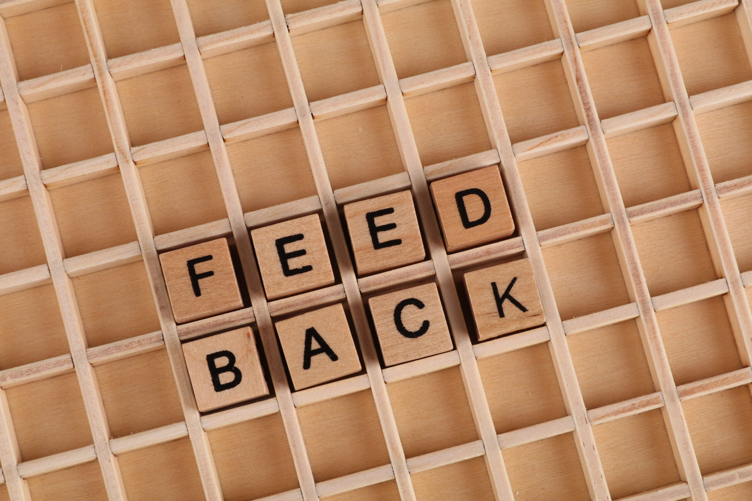 Wooden letter blocks spelling 'Feedback' on a wooden grid surface.